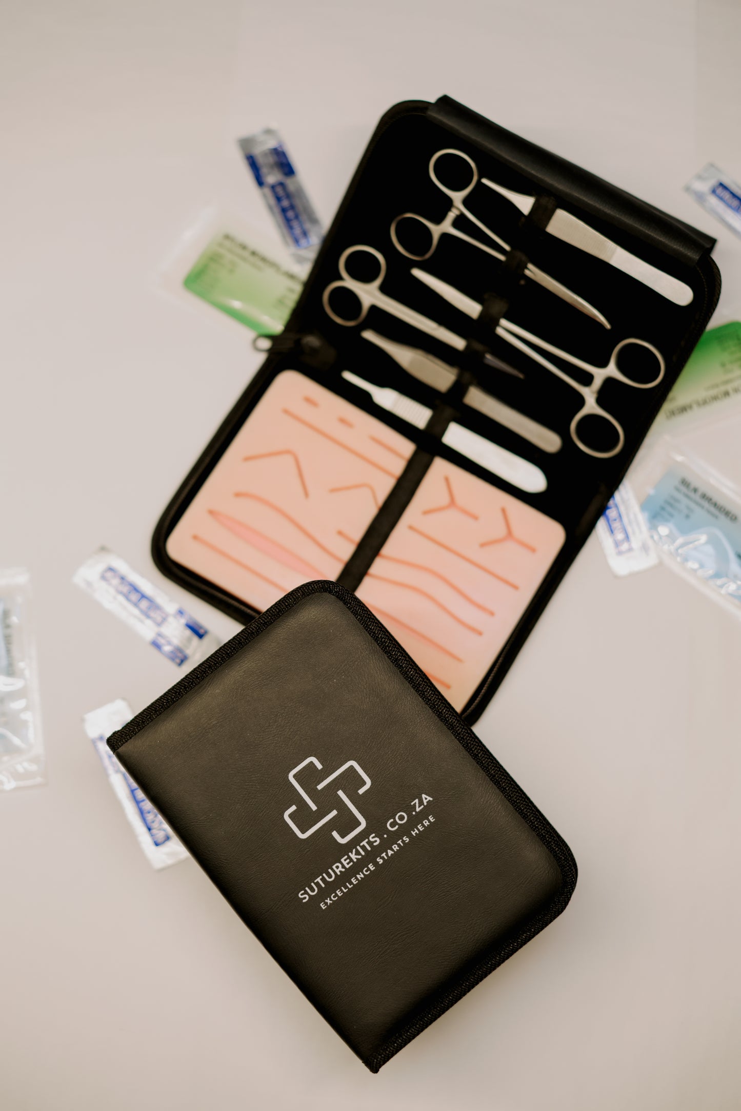 Suture kit with tools and swabs on a light surface, featuring the Suture Kit Co.ZA logo.