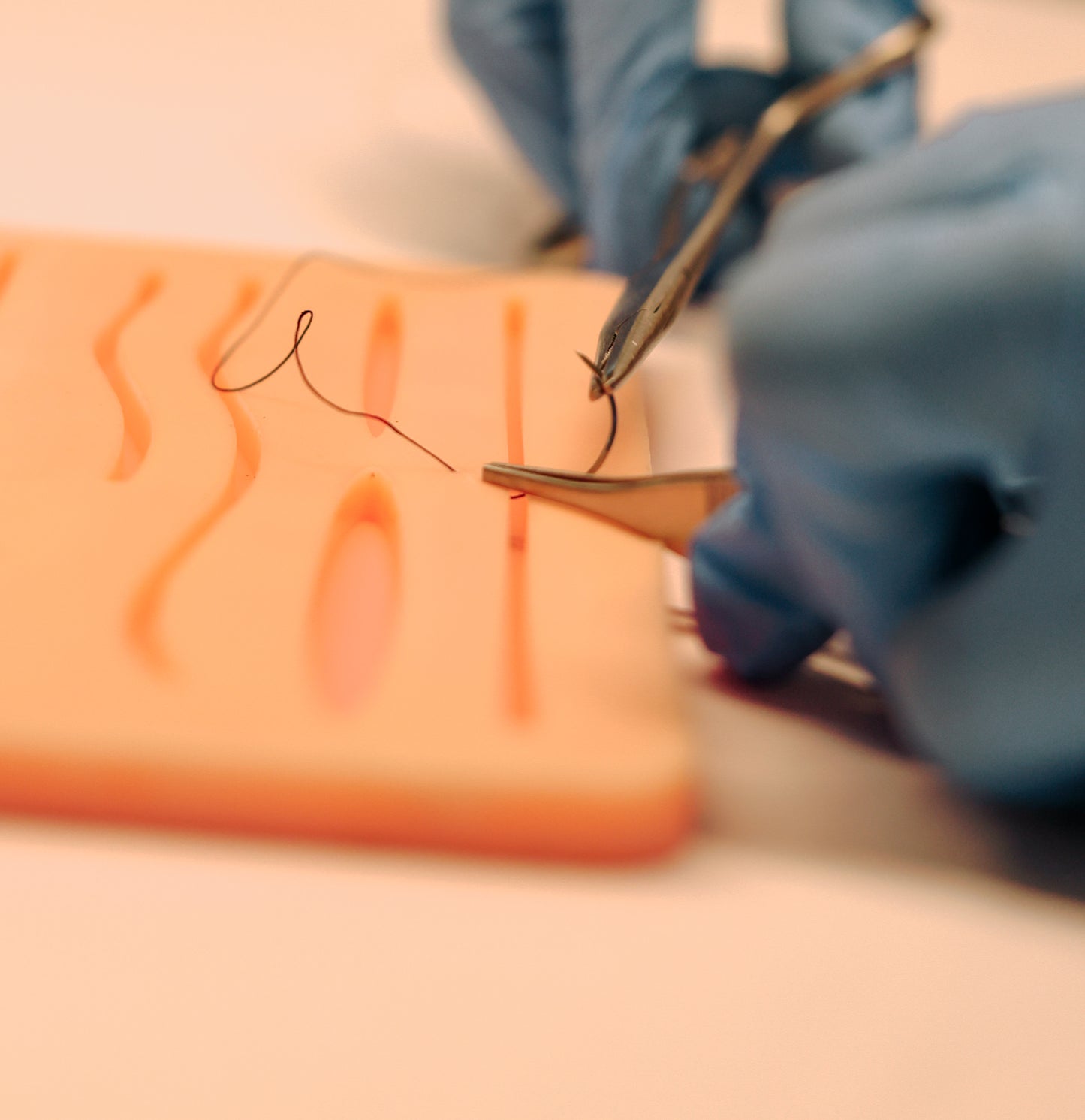 Close-up of a hand holding tweezers with a needle over an orange surface.