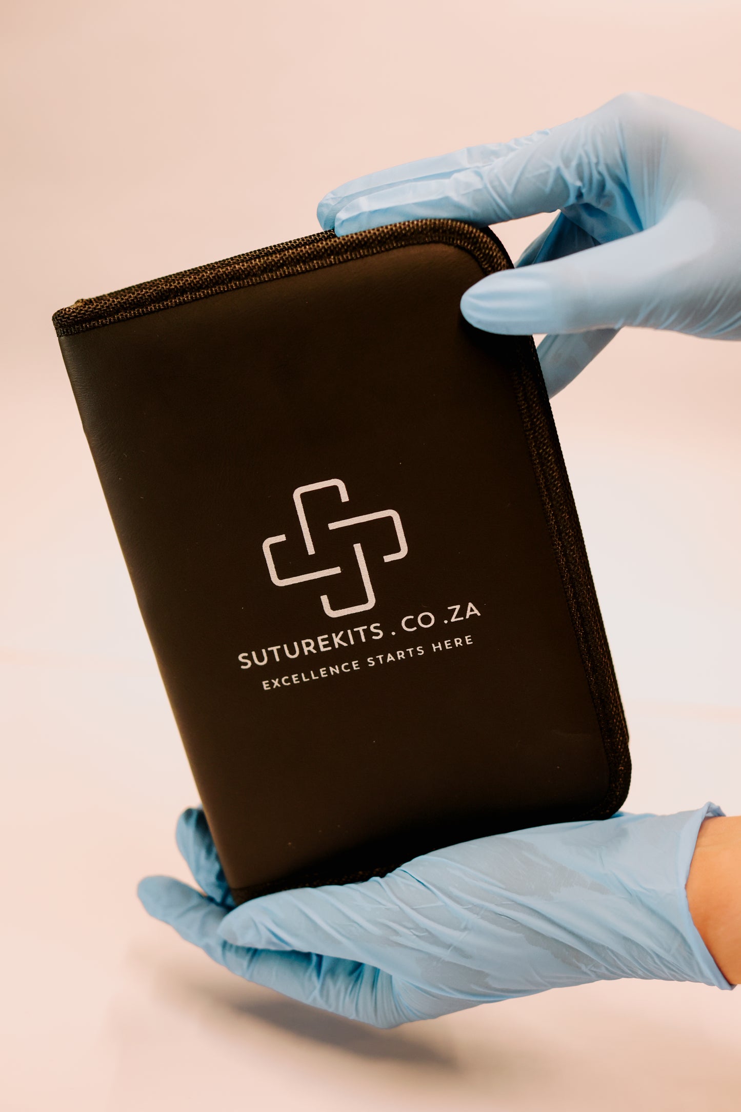 Black zippered pouch held by hands in blue gloves with 'Suturekits.co.za' branding.